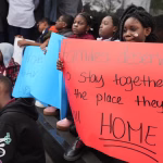 A young person at a rally holds a sign that reads 'families deserve to stay together in the place they call home.'